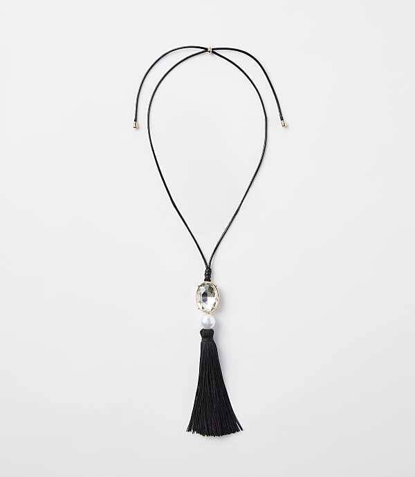 A black tassel necklace with a clear gem and pearl hangs against a plain white background.