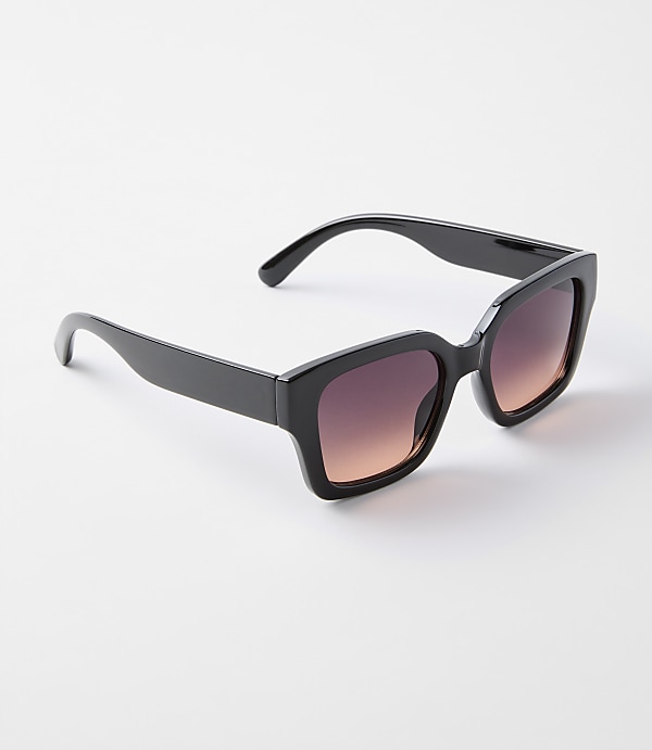 A pair of black, oversized sunglasses with gradient lenses rests on a plain white background.