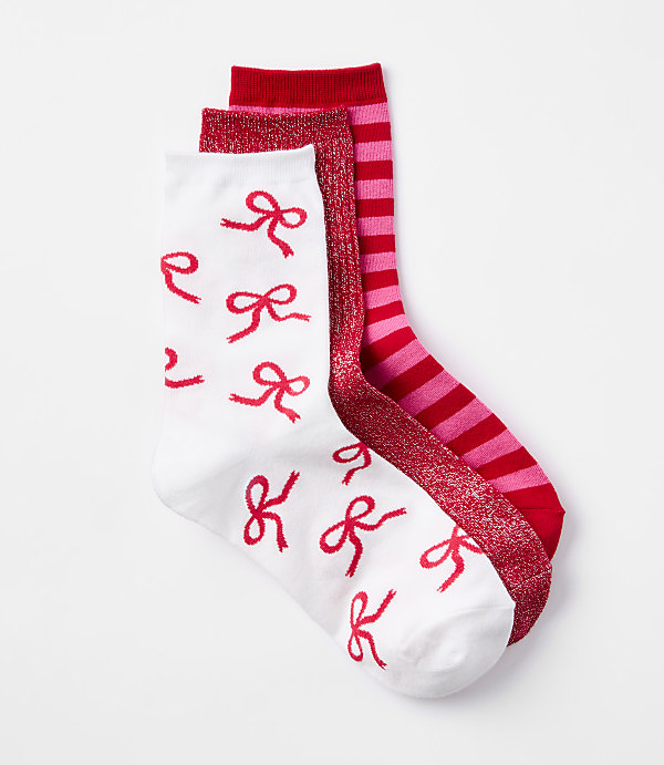 Three pairs of red and pink socks, one with a white background and red bows, another with red and pink stripes and glitter, and a solid red one, are neatly arranged against a plain white background.