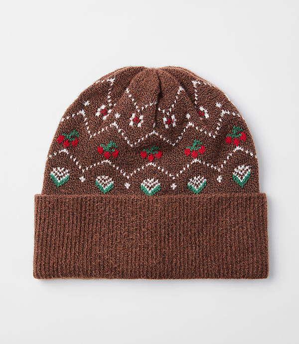A brown knitted beanie with a festive fair isle pattern of red cherries and green leaves sits against a plain white background.