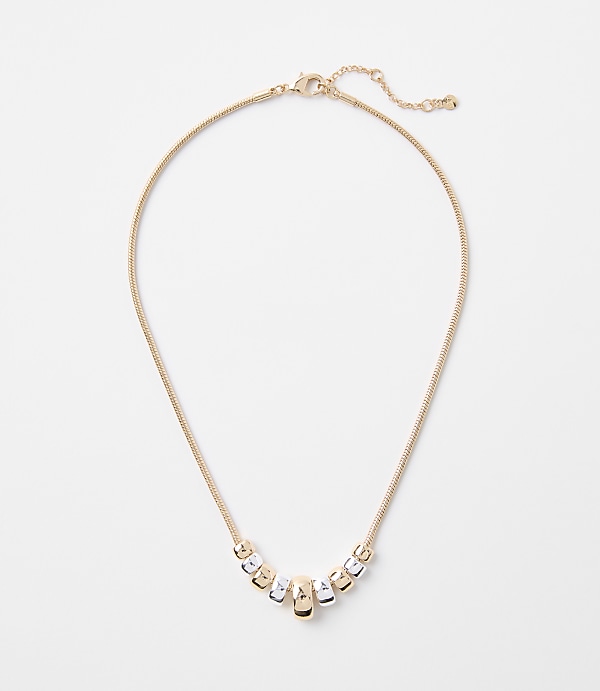 A delicate gold chain necklace with a series of alternating gold and silver cylindrical beads rests on a plain white background.