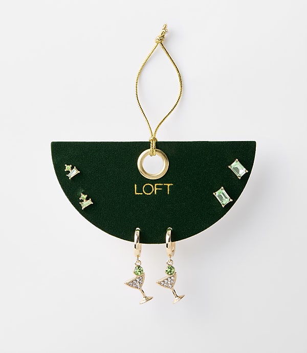 A set of green jeweled earrings, including martini glass and stud styles, are displayed on a dark green card with a gold loop and string against a plain white background.