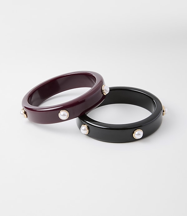 Two chunky bangles, one deep red and the other black, are adorned with small pearls and gold accents, set against a plain white background.