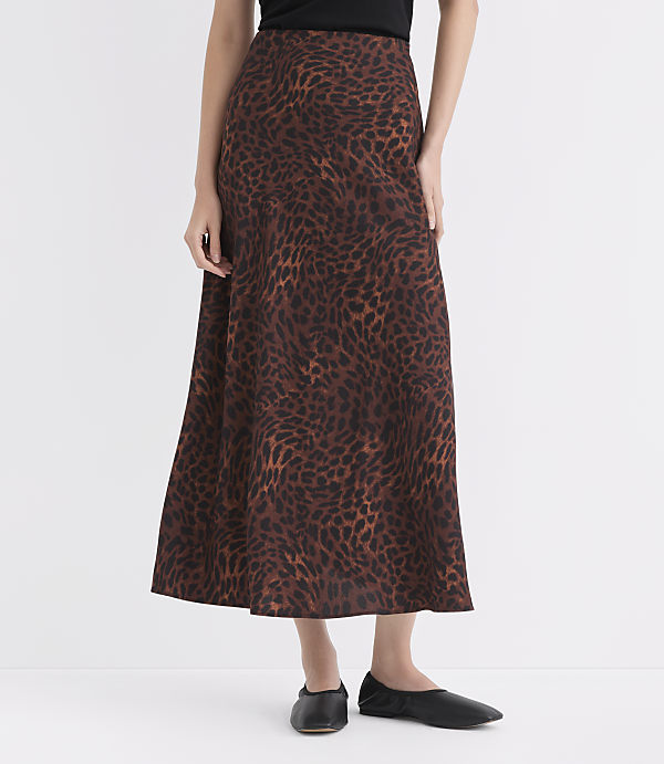 A woman in a leopard print skirt and black flats stands against a plain white background.