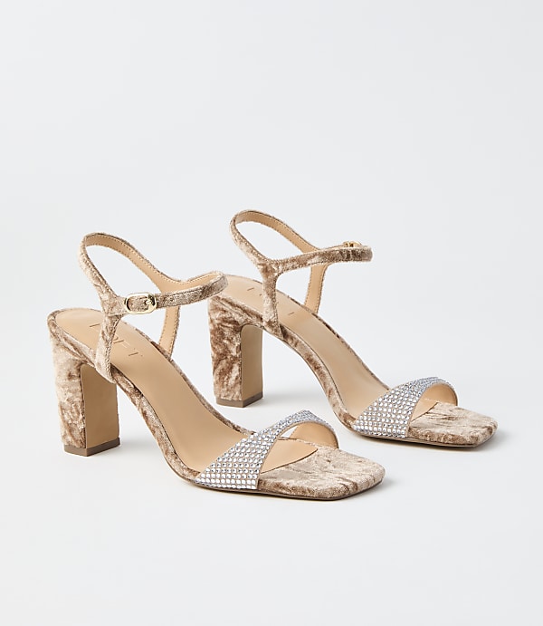 A pair of crushed velvet block heels with rhinestone straps rests on a plain white background.