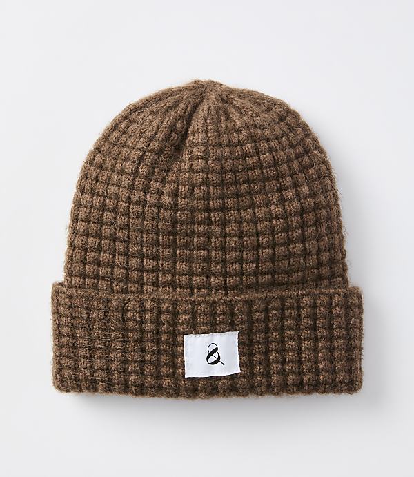 A brown waffle-knit beanie with a white tag featuring a black ampersand sits against a plain white background.