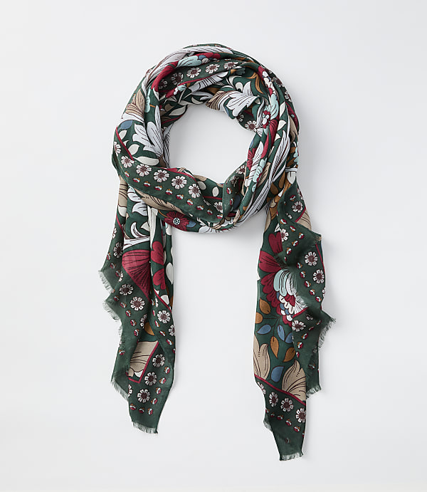 A green scarf with a floral and book pattern hangs against a plain white background.