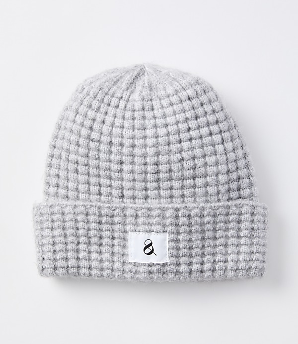 A light gray knitted beanie with a waffle knit pattern and a white tag with a black ampersand sits on a plain white background.