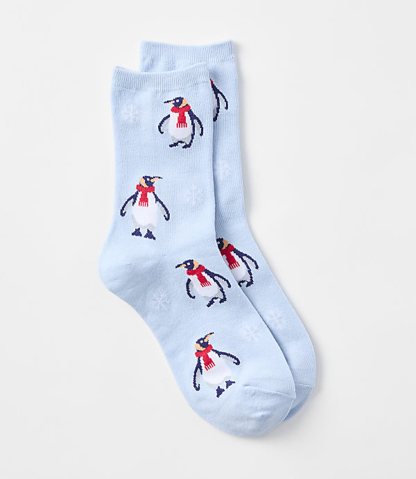 A pair of light blue socks with a pattern of penguins wearing red scarves and snowflakes are laid out against a plain white background.