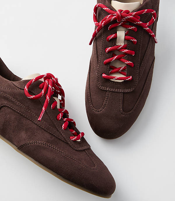 Two brown suede sneakers with red and white laces are displayed against a plain white background.