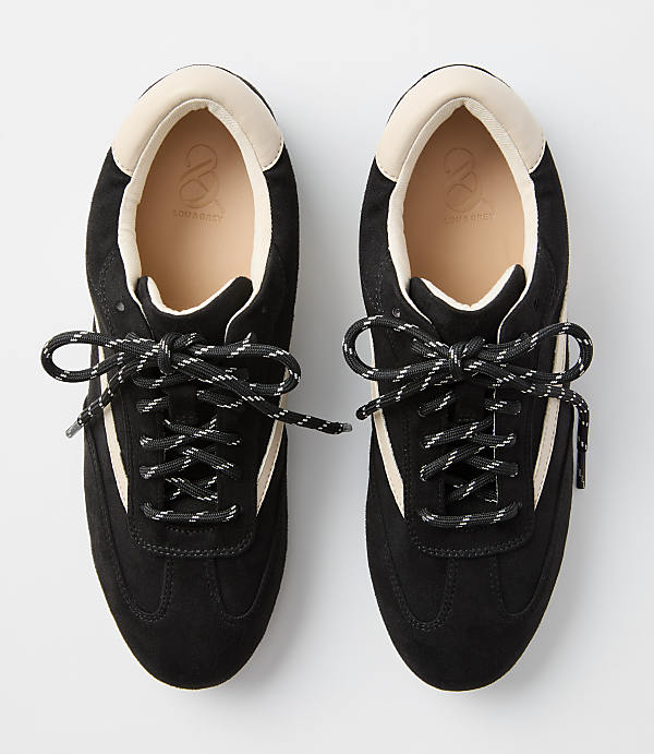 A pair of black suede sneakers with cream accents and black and white laces are laid out on a plain white background.