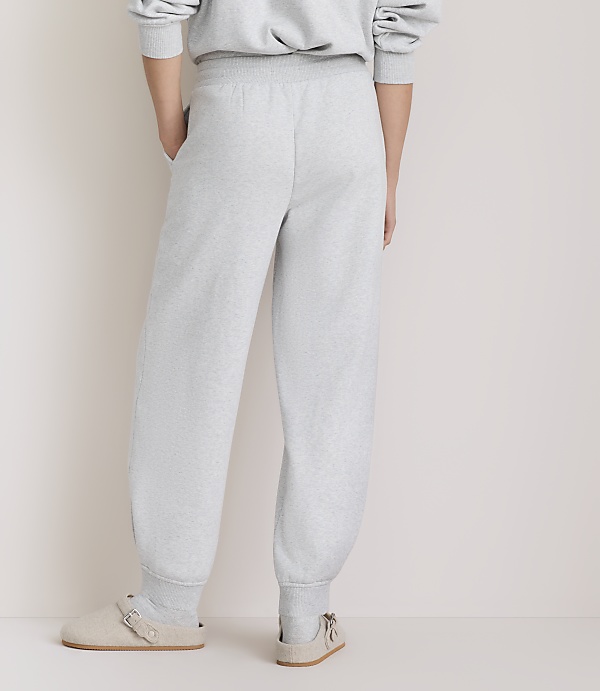A person wearing light gray sweatpants and clogs stands against a plain, light-colored background.