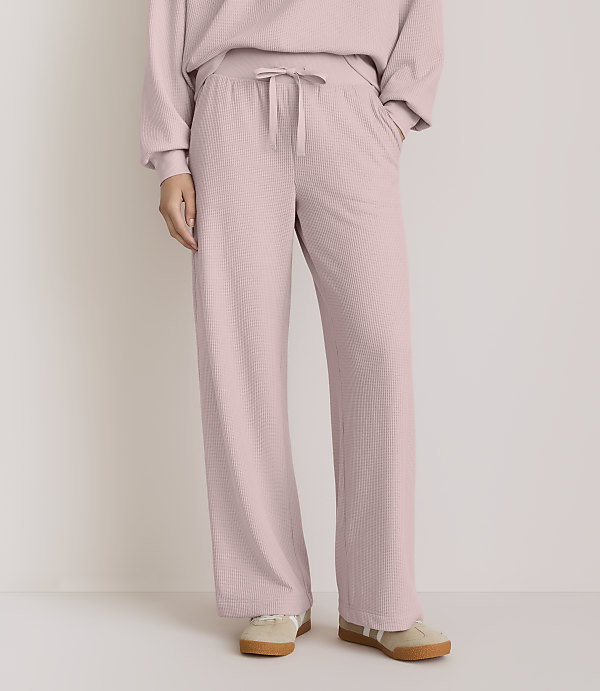 A person wearing pink ribbed lounge pants and sneakers stands against a plain, light-colored background.