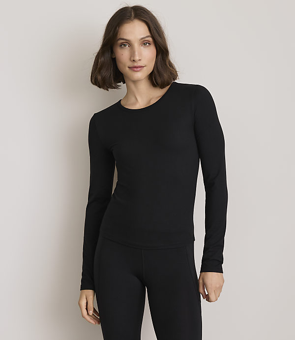 A woman in a black long-sleeved shirt and leggings stands against a plain gray background.
