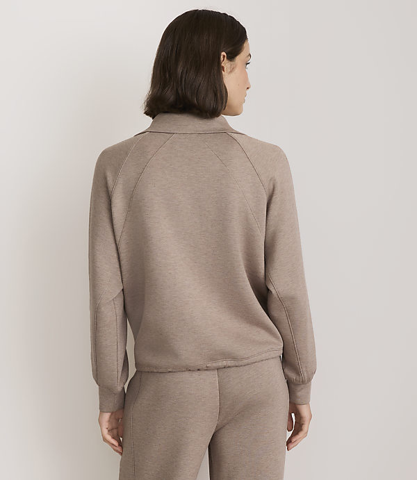 A woman in a taupe collared sweatshirt and matching pants stands against a plain white background.
