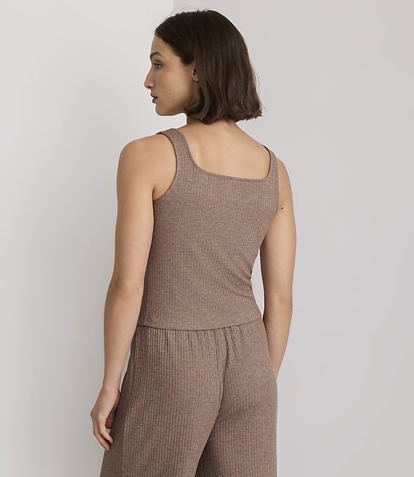 A woman in a brown ribbed tank top and matching pants stands against a plain, light-colored background.