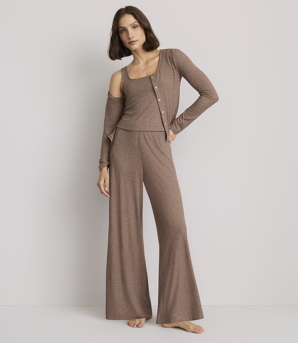 A woman in a brown ribbed loungewear set stands against a plain gray background.