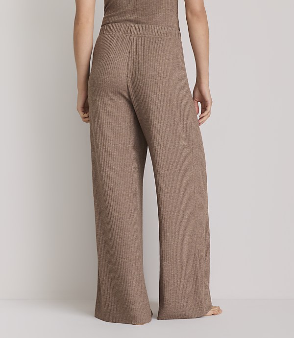 A person stands in ribbed brown wide-leg pants and a matching top against a plain white background.