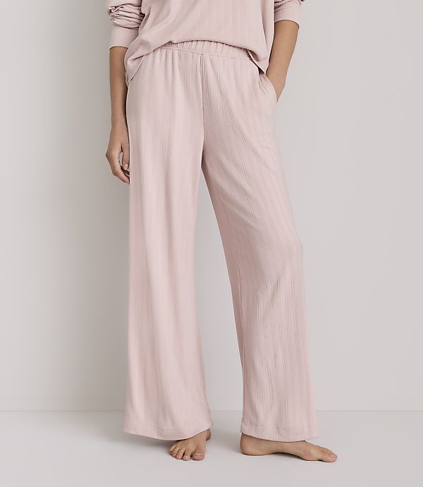 A person stands in pale pink ribbed pajama pants with their hands in their pockets against a plain white background.