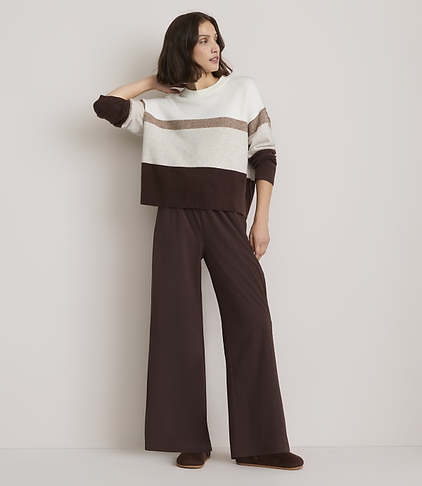 A woman in a striped sweater and wide-leg pants stands against a plain white background.