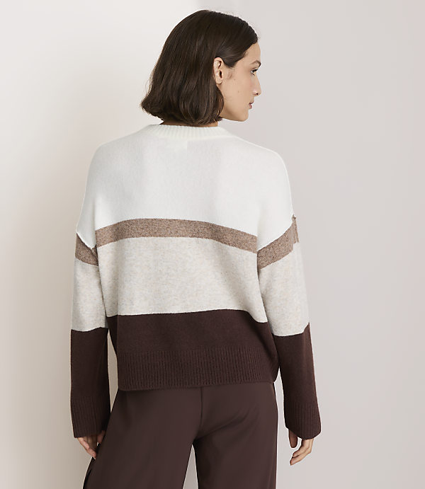 A woman in a striped sweater stands against a plain, light-colored background.