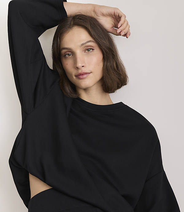 A woman in a black sweatshirt poses with her arm raised against a plain white background.