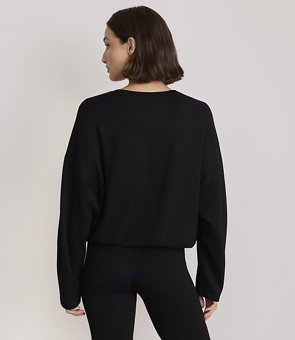 A woman in a black sweater and leggings stands against a plain, light-colored background.