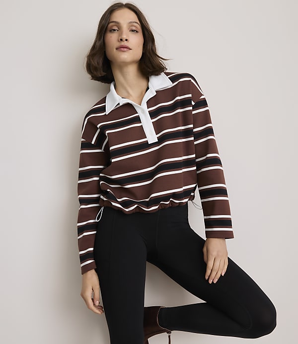 A woman in a striped rugby shirt and black leggings poses against a plain background.