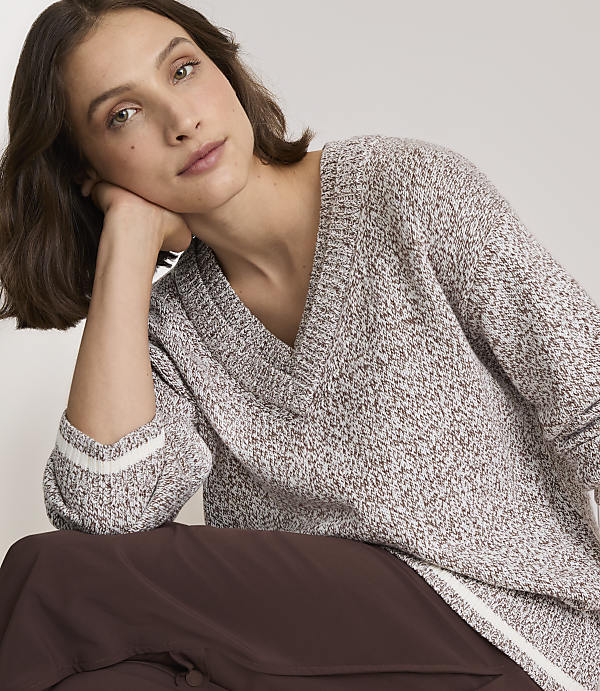 A woman in a speckled v-neck sweater rests her head on her hand against a plain background.