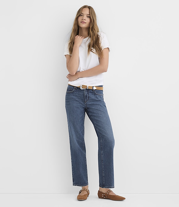 A young woman in a white t-shirt and blue jeans stands against a plain white background.