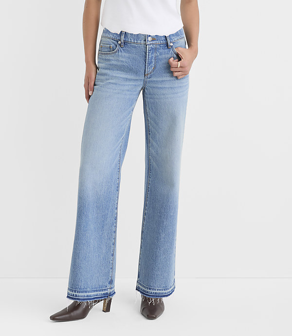 A person stands in light-wash flared jeans with frayed hems and dark pointed-toe heels against a plain white background.