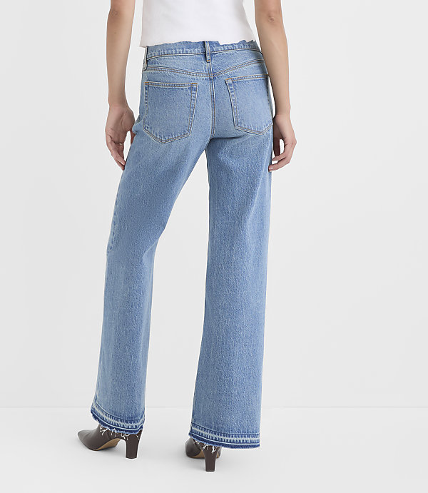 A person wearing light-wash flared jeans with frayed hems stands against a plain white background.