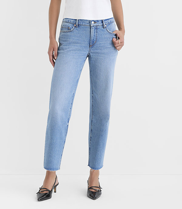 A person wearing light-wash denim jeans and black heels stands against a plain white background.