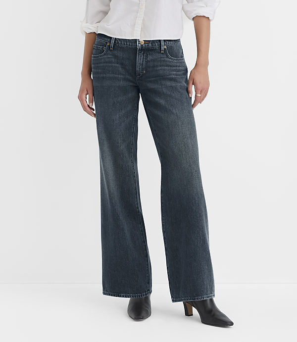 A person wearing dark wash wide-leg jeans and black heeled boots stands against a plain white background.