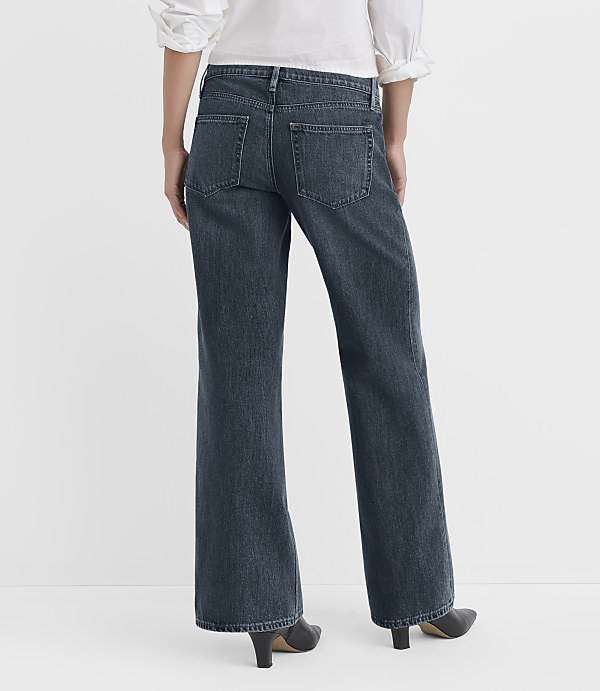 A person wearing dark wash flared jeans and a white top stands against a plain white background.