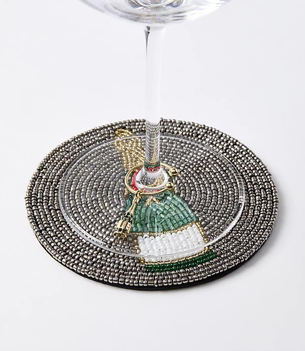 A beaded coaster with a festive bottle charm encircles the stem of a wine glass against a plain white background.
