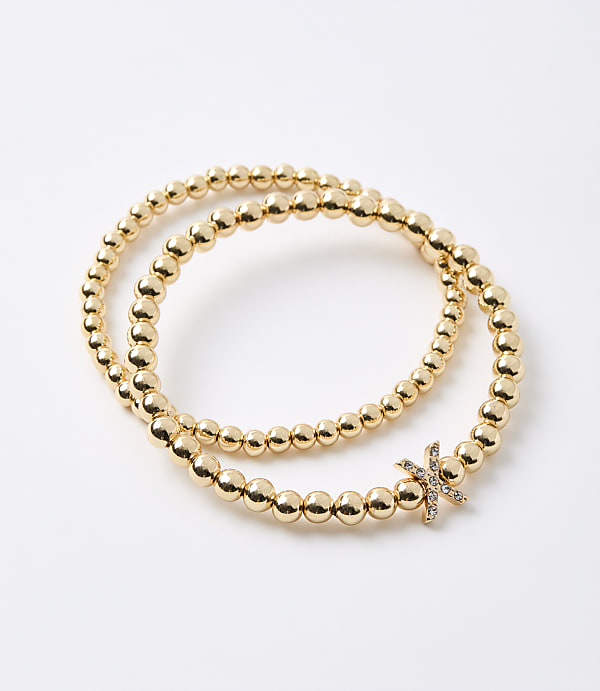 Two gold beaded bracelets, one with a diamond-studded initial "K" charm, are arranged on a plain white background.
