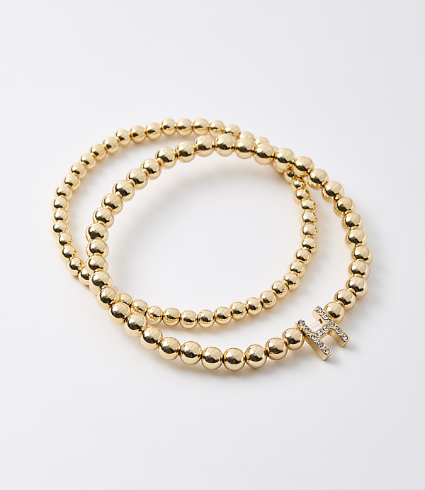 A gold beaded bracelet with a diamond-encrusted initial "H" rests on a plain white background.