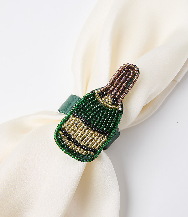 A beaded champagne bottle napkin ring adorns a cream-colored cloth against a plain white background.