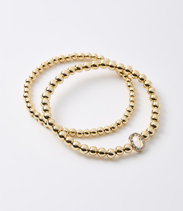 Two gold beaded bracelets, one with a diamond-encrusted oval charm, lie on a plain white background.