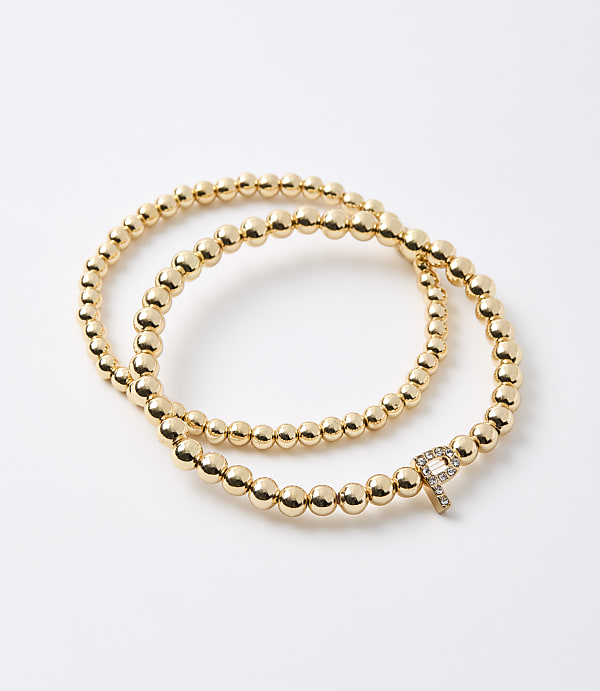 A gold beaded bracelet with a diamond-encrusted "P" charm is laid out on a white background.
