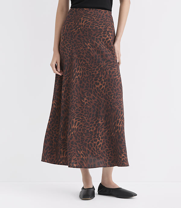 A woman in a leopard print skirt and black flats stands against a plain white background.