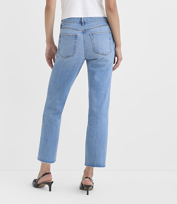 A person wearing light blue jeans and black heels stands against a plain white background.