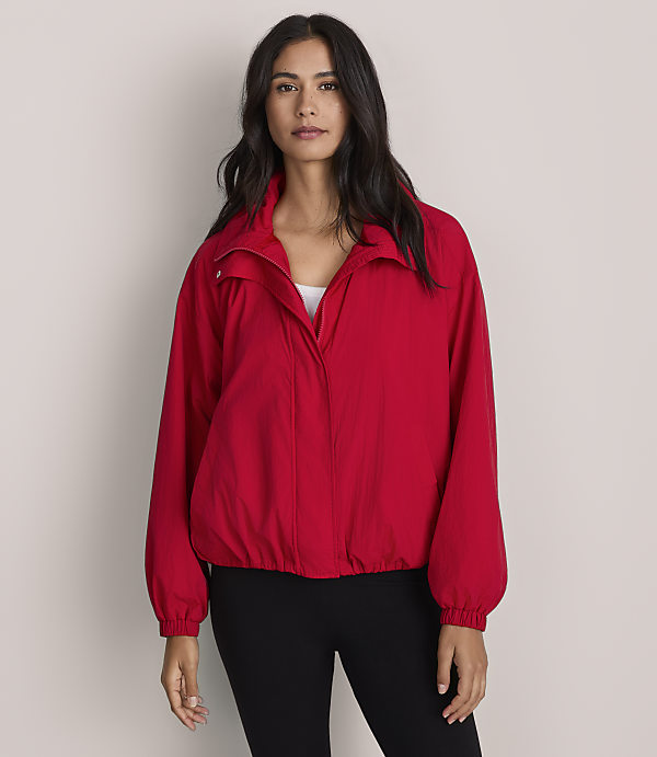 A woman in a red jacket and white tank top stands against a plain gray background.