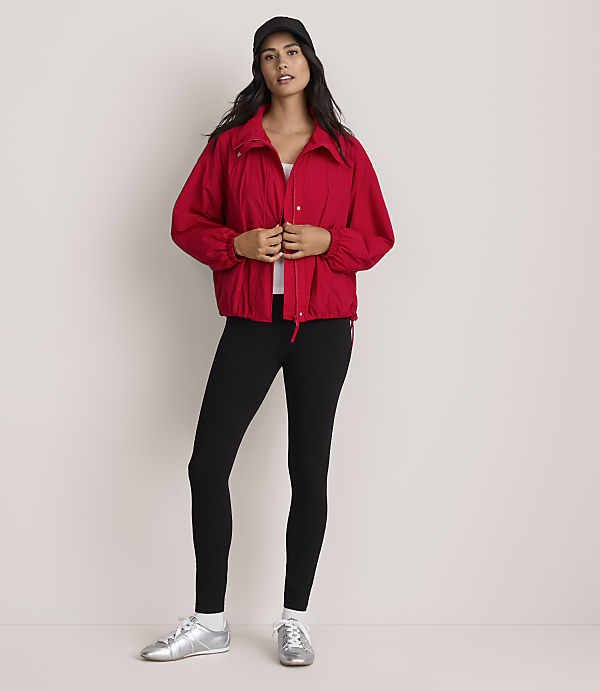 A woman in a red jacket and black leggings sits against a plain gray background.