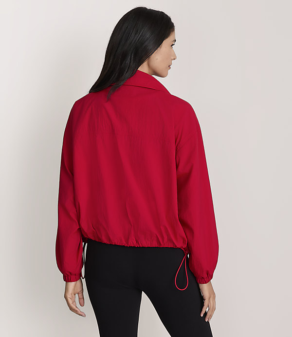 A woman in a red jacket and black leggings stands against a plain gray background.
