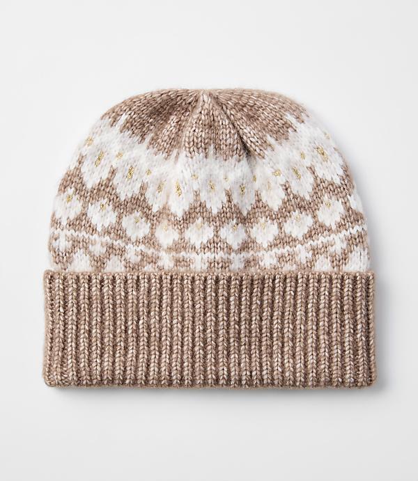 A knitted beanie with a ribbed brim in a light brown color is in the foreground, while the background is a plain white surface.