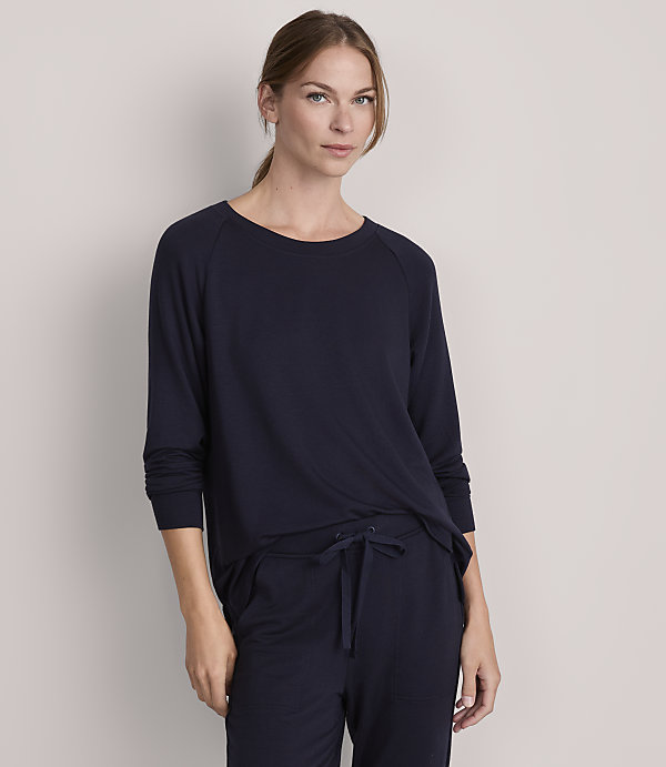 A woman in a navy blue long-sleeved shirt and matching pants stands against a plain gray background.