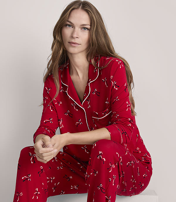 A woman in red pajamas with a bow pattern sits against a plain gray background.