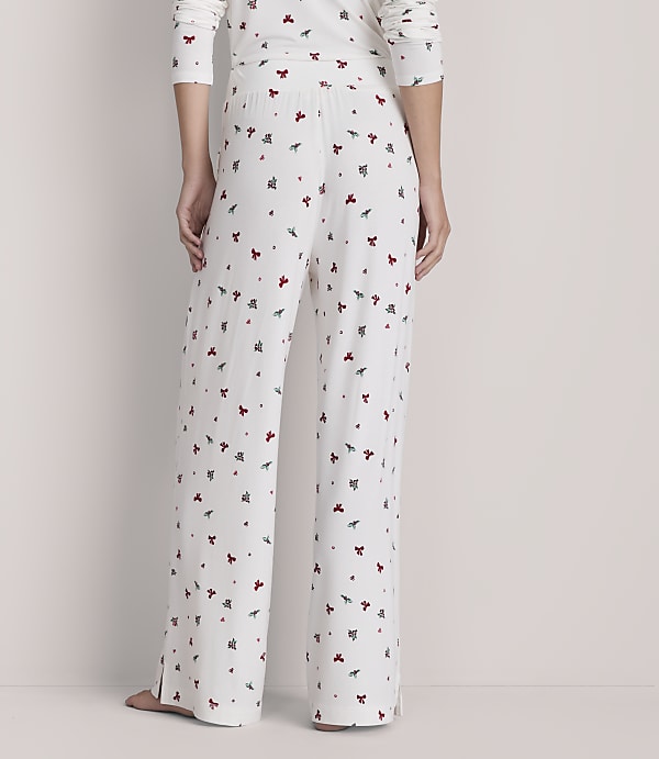 A person stands in white pajamas with a red and green holly pattern, against a plain, light-colored background.